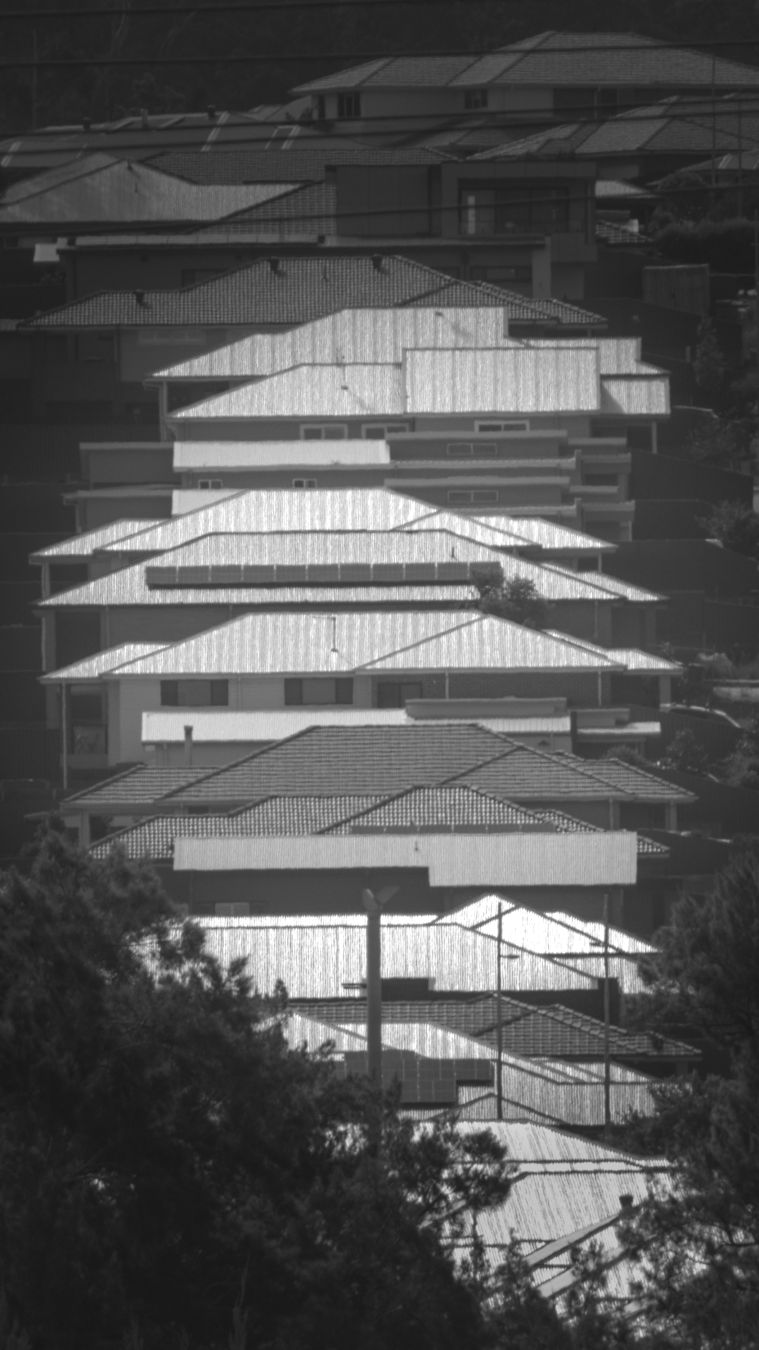A black and white photo of a row of shiny roof tops going up a hill.