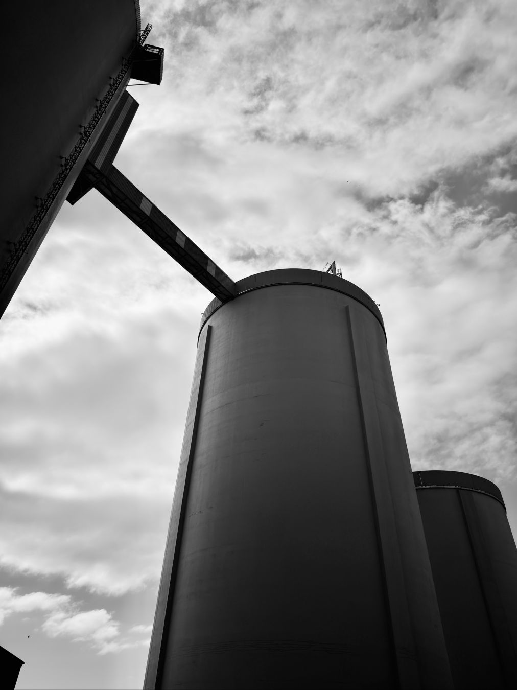Black and white photograph looking up at three large silos. Two silos are joined together at their tops by a small connecting structure.