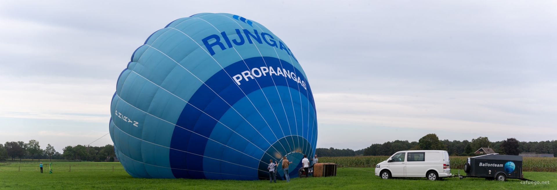Panorama of a blue hot air balloon being inflated in a field.