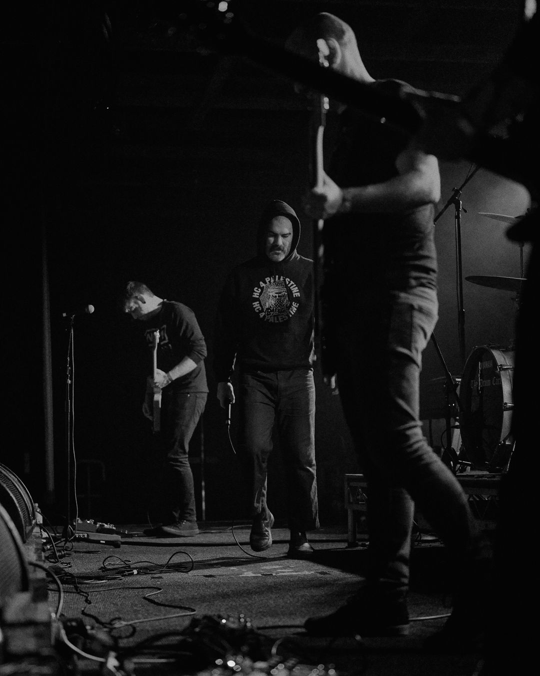 A black and white image from side of stage showing multiple members of slowcut. HC for Palestine. ✊