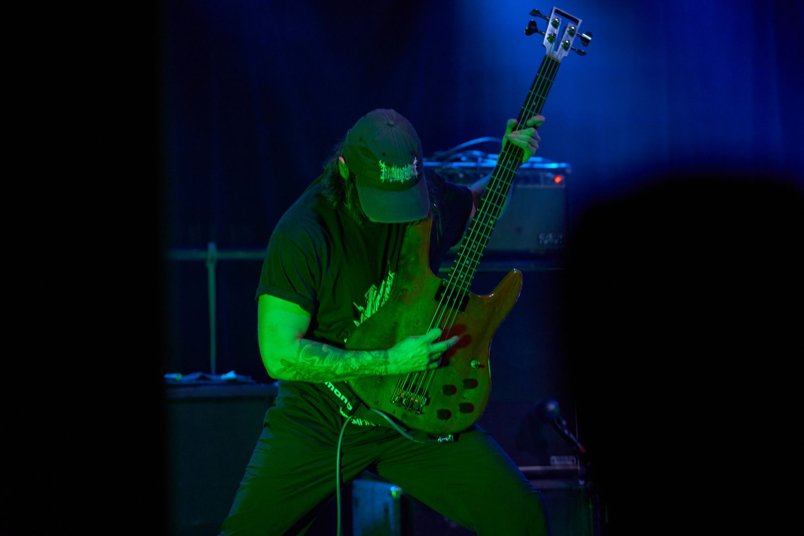 Bassist pulls a powerful bass stance to blast powerful riffs, washed in green light.