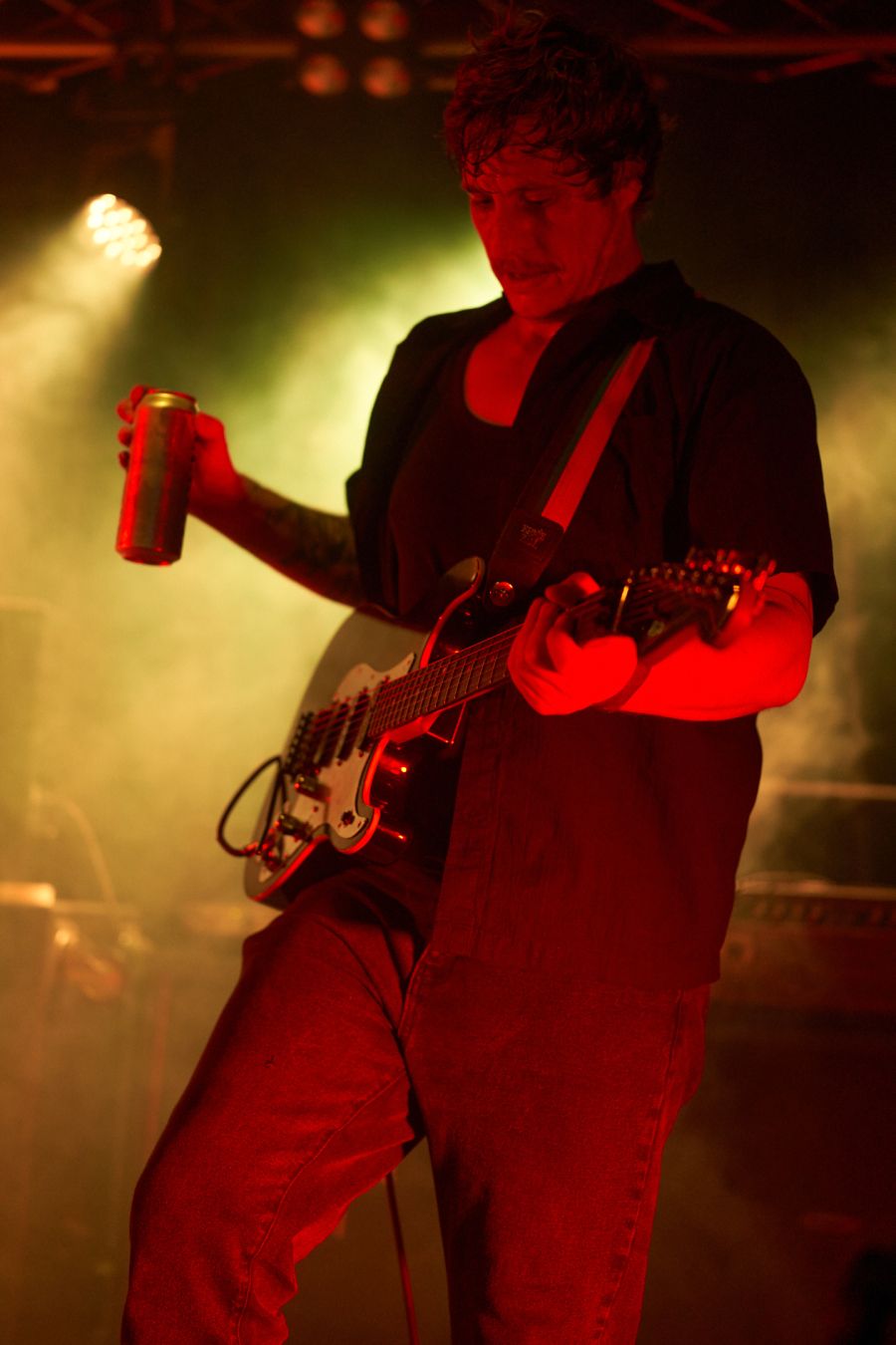 Totally Unicorn guitarist takes a well earned drink break, covered in red light with yellow haze behind.