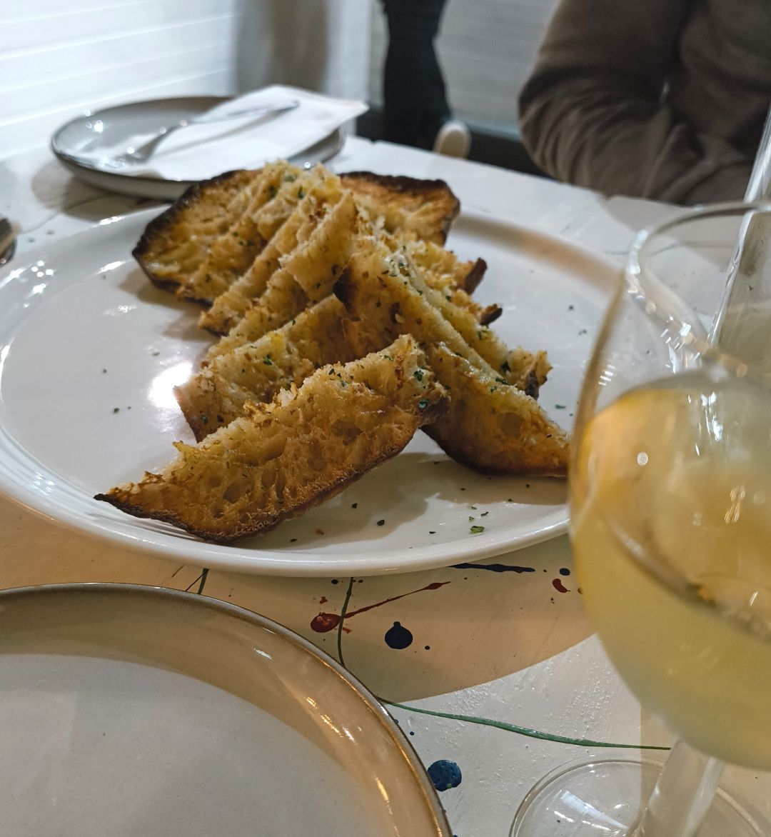 Garlic bruschetta arranged on a plate, with a glass of the house white wine in the foreground