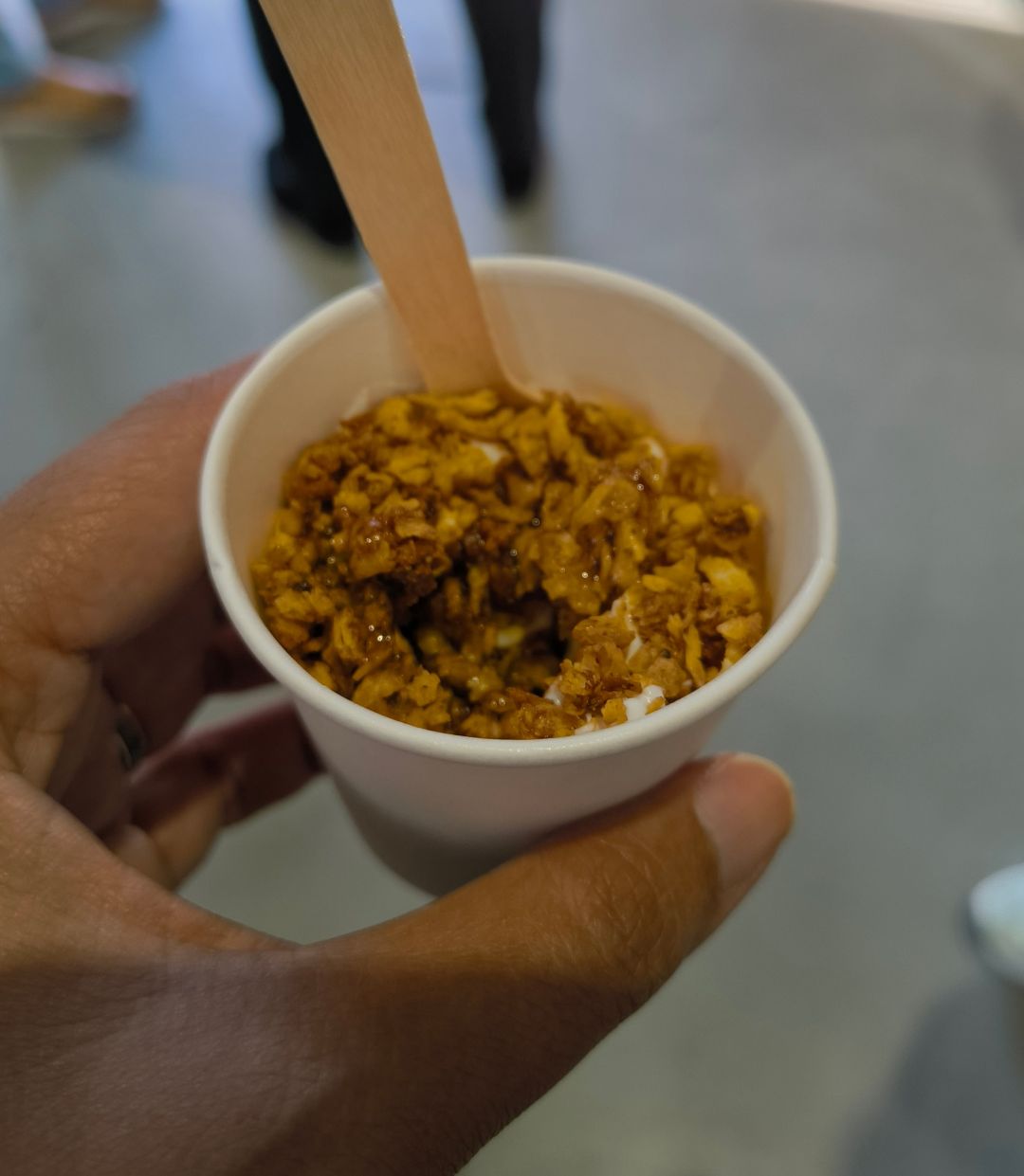 A small cup of yoghurt topped with sweetened protein crumble and a drizzle of maple syrup.