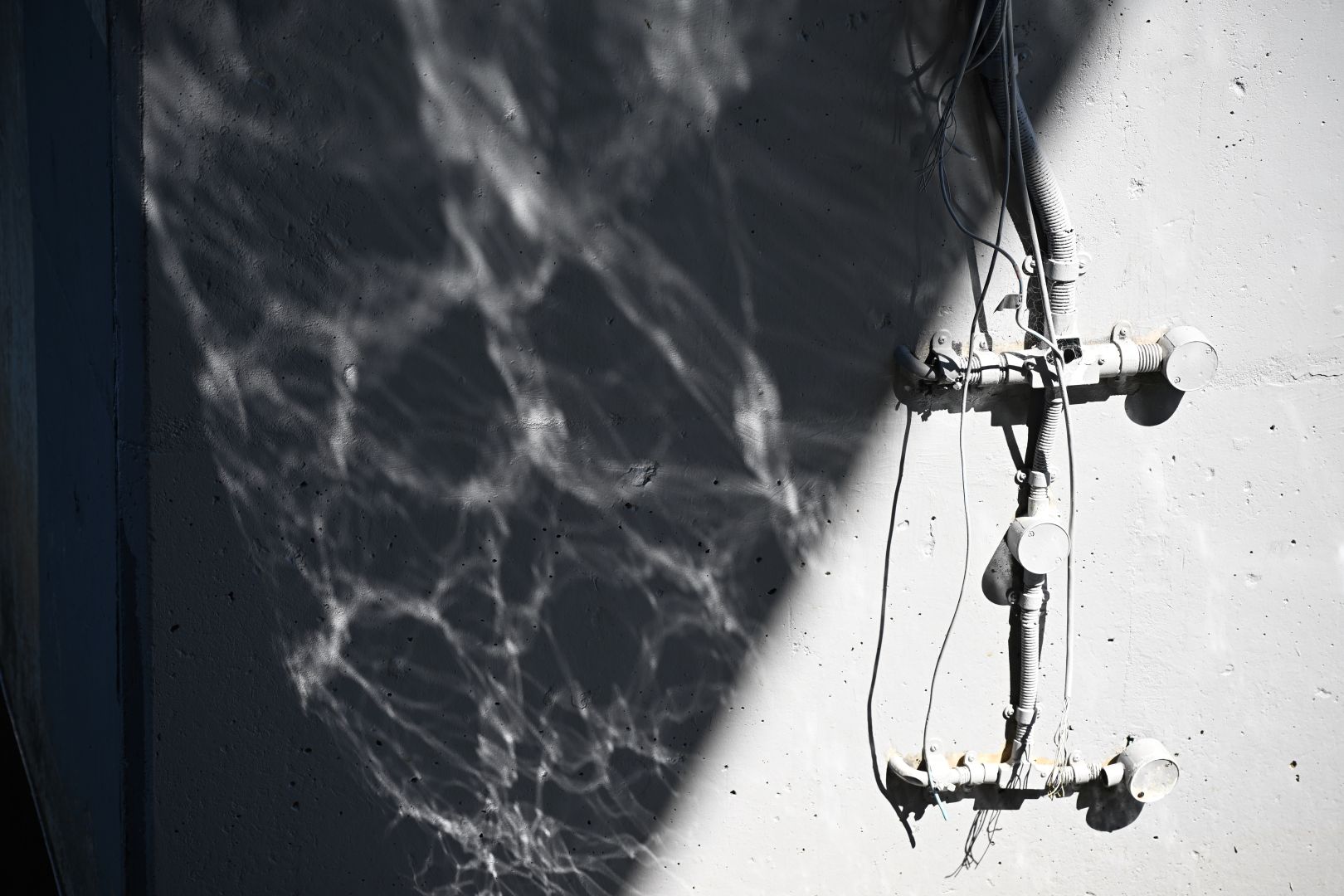 hoses and wires in light sharply contrasted by reflections of water (caustics) in darkness with a striking diagonal divider that appears quite unrealistic (but is an actual photo)